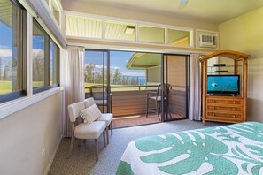 Une chambre d’hôtel avec un balcon, une télévision, un lit recouvert d’une courtepointe à motifs verts et blancs, et une chaise avec un coussin.