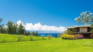 Une maison avec vue sur l’océan, entourée de verdure et d’arbres.