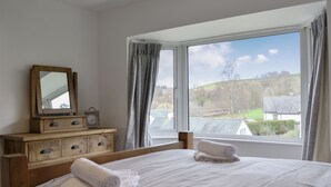 Camera da letto con due letti, una cassettiera, uno specchio e una finestra vista casa e paesaggio.