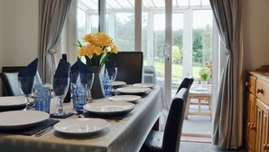 Zona pranzo con tavolo apparecchiato per quattro persone, un vaso con fiori gialli e vista su un giardino attraverso ampie finestre.