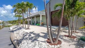 A modern building with a covered outdoor area, palm trees, and a sandy ground.