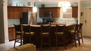 A kitchen with wooden cabinets, a refrigerator, a microwave, and a bar area with bar stools.