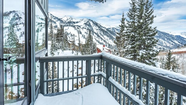 Un balcone con pavimento innevato e vista su montagne e alberi coperti di neve.
