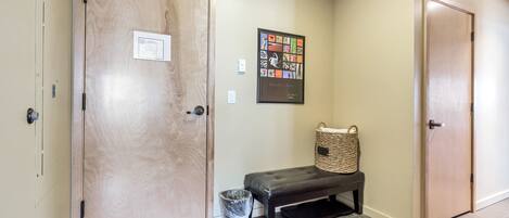 A hallway with two wooden doors, a bench, a trash can, and a framed artwork on the wall.