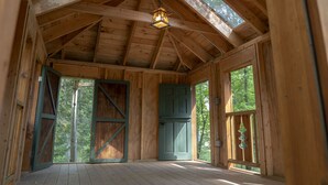Interior de una cabaña de madera con techo alto, ventanas grandes y una puerta con marco verde.