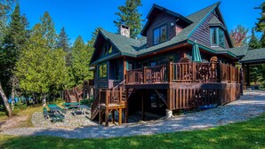 Una cabaña de troncos con terraza, mobiliario exterior y una chimenea de piedra.