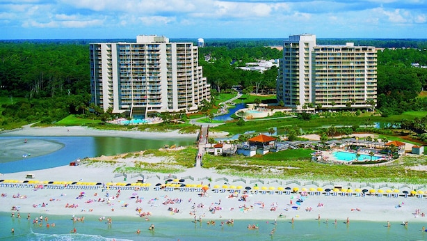 Un hôtel situé en bord de mer, composé de plusieurs immeubles de grande hauteur, doté d’un espace piscine et d’une plage de sable.