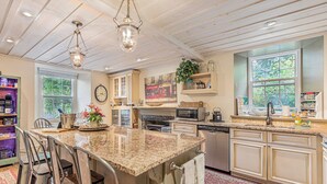 A kitchen with a granite island, wooden cabinets, a microwave, and a large window.