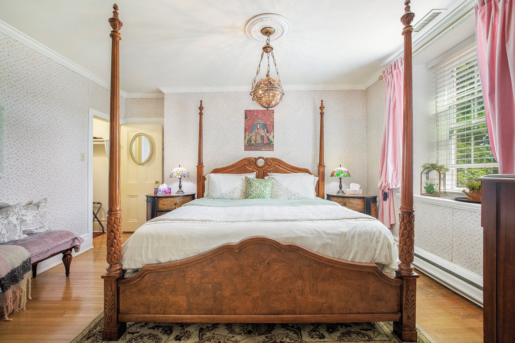 A four-poster bed with a wooden headboard, a hanging chandelier, and a floral-patterned rug.