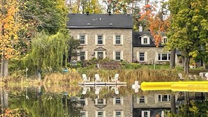 A stone building with a symmetrical facade, a pond in front, and autumn foliage in the background.