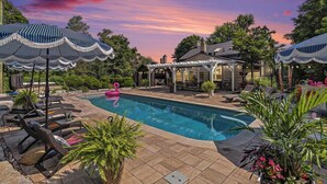 A swimming pool with lounge chairs and umbrellas, surrounded by greenery and a gazebo.