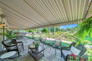 An outdoor patio with wicker furniture, a wooden table, and a view of a garden.