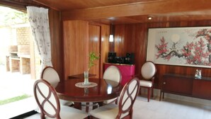 Une salle à manger aux murs lambrés, avec une table ronde, quatre chaises, un vase avec une plante et un tableau accroché au mur.
