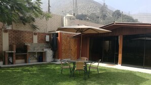 Un jardin avec un espace barbecue, une table et des chaises, et une terrasse couverte.