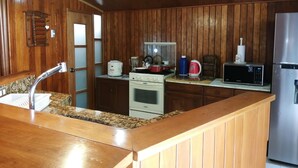 Une cuisine avec des lambris en bois, un plan de travail en granit, un réfrigérateur en acier inoxydable, un four à micro-ondes, une cuisinière et un évier.