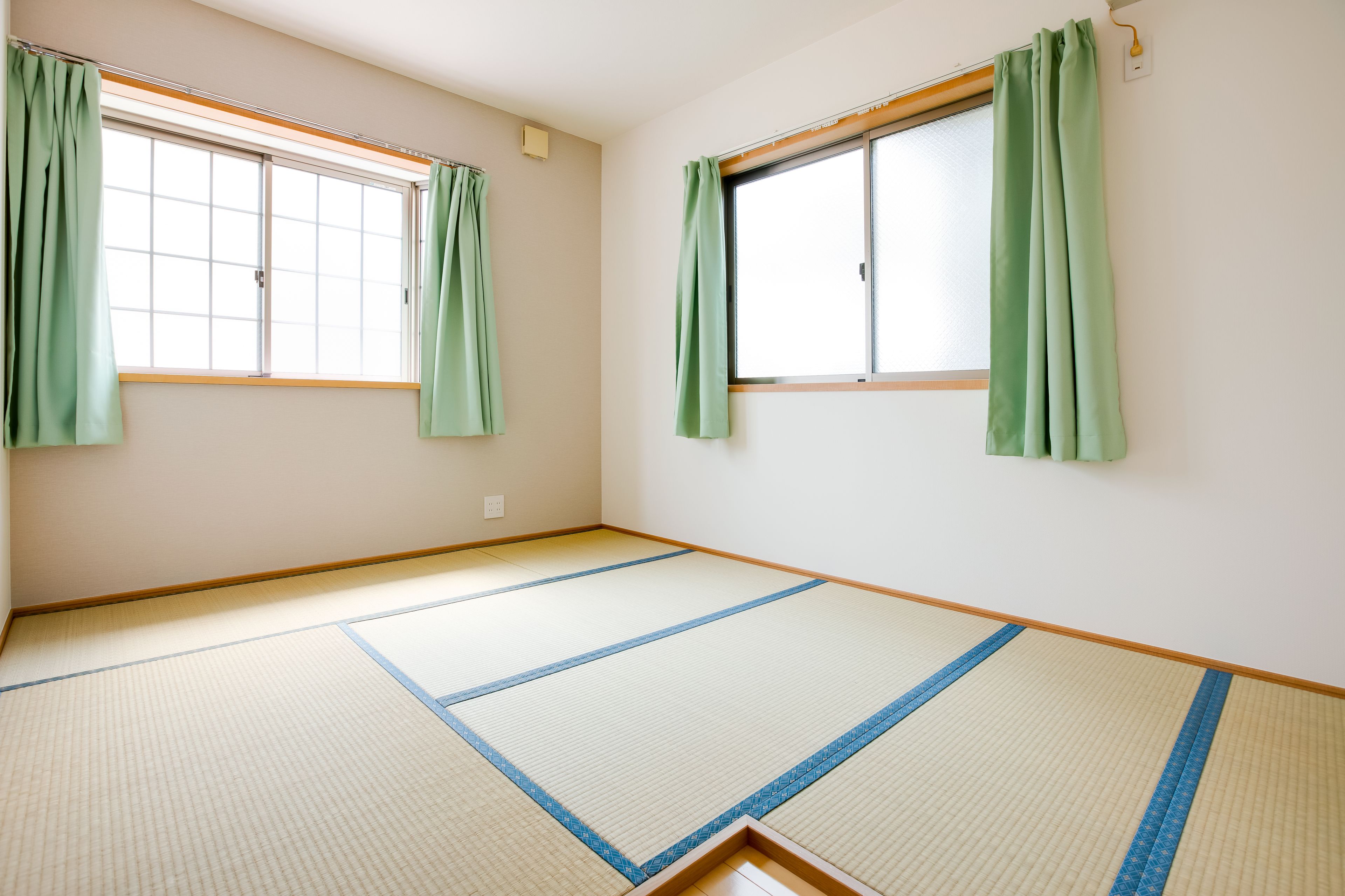 Quarto com piso de tatame, duas janelas com cortinas verdes e moldura de madeira.