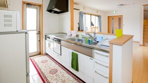 Une cuisine moderne avec des meubles blancs, un plan de travail en acier inoxydable, un lave-vaisselle encastré et une grande fenêtre avec des rideaux.