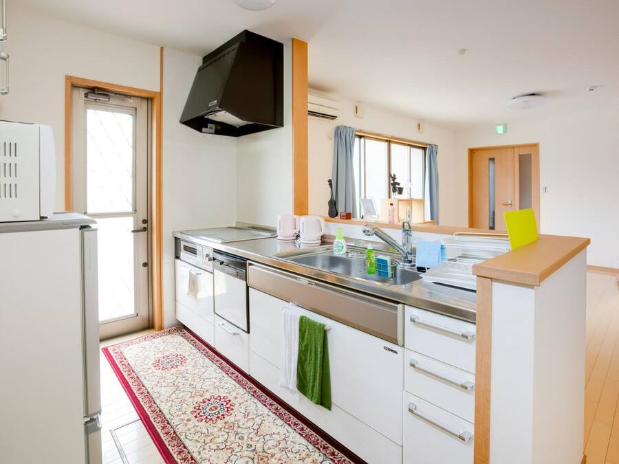 Una cocina moderna con armarios blancos, encimera de acero inoxidable, lavavajillas integrado y un amplio ventanal con cortinas.