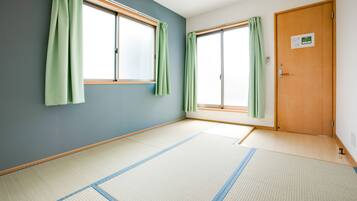 A room with tatami flooring, two windows with green curtains, and a wooden door.