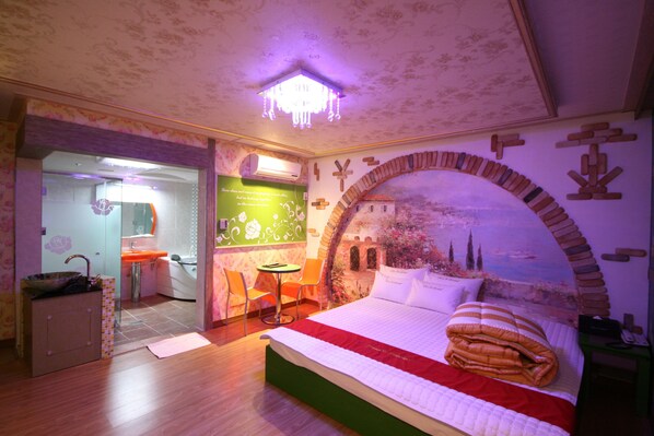 A bedroom with a bed, a small table, two chairs, a sink, and a mirror.