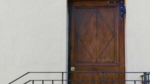 Une porte en bois avec un portail en métal, un petit balcon doté d’une rambarde en métal et un luminaire fixé au mur au-dessus de la porte.