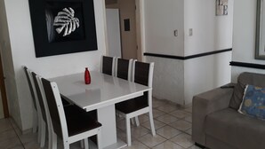 Een eethoek met een witte tafel en stoelen, een rode vaas en een kunstwerk in een lijst aan de muur.
