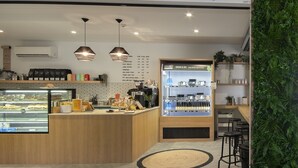 Een net café interieur met een menubord, koffiemachines en een vitrine.