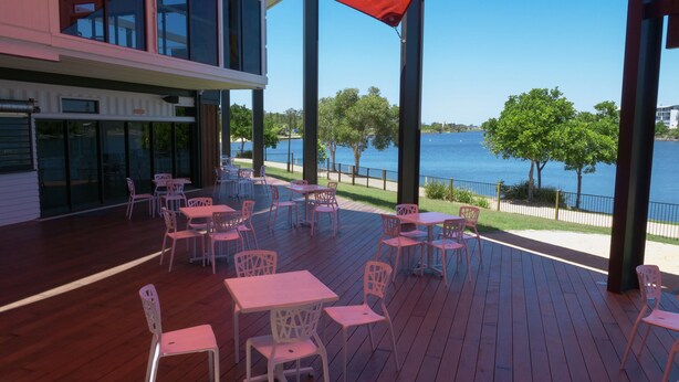 Een terras buiten met tafels en stoelen, met uitzicht op water en bomen.