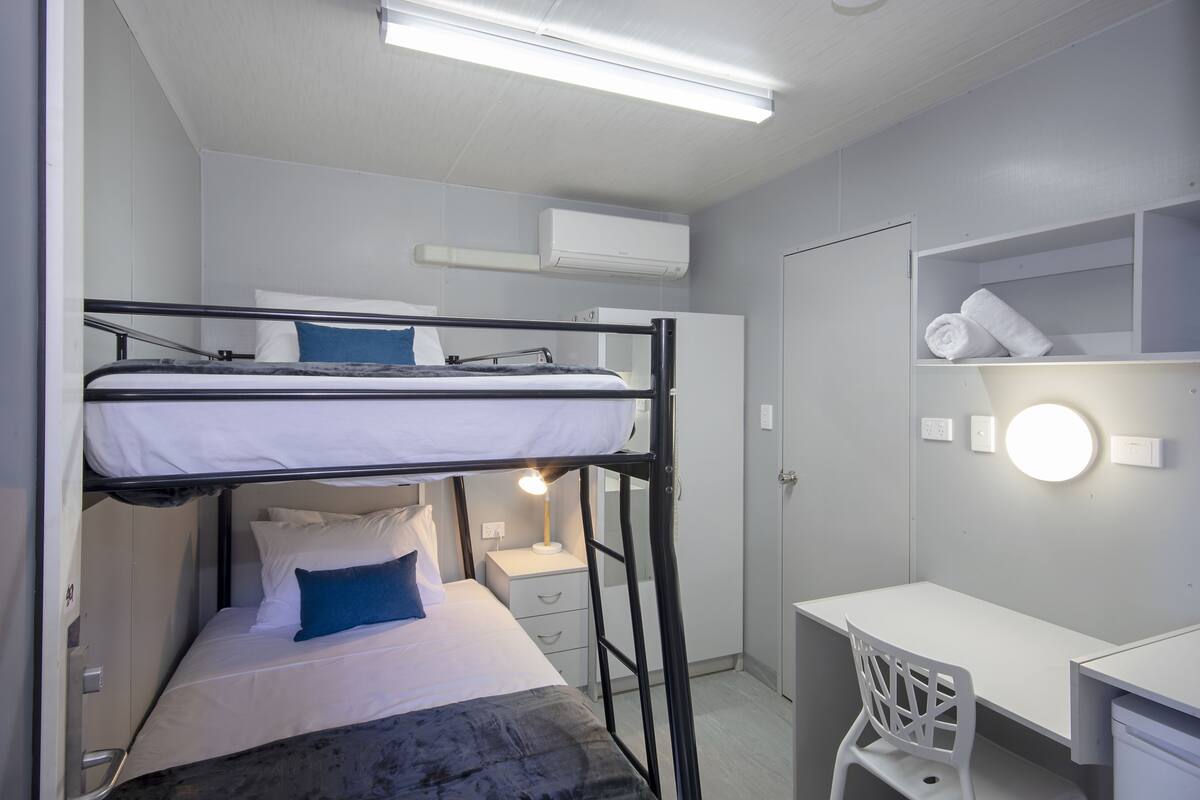 Un lit superposé avec un bureau et une chaise, une armoire blanche et un miroir rond avec éclairage.