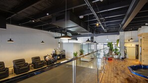 Een moderne kantoorruimte met een lange receptiebalie, zwarte lederen stoelen, een glazen balustrade en een houten vloer.