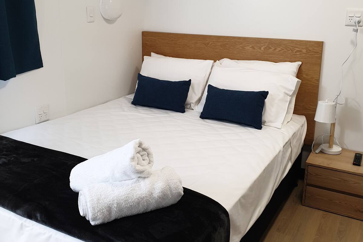 Un lit bien fait, avec des oreillers blancs et bleu foncé, une serviette blanche et une tête de lit en bois.