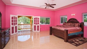 A bedroom with pink walls, a wooden bed, a ceiling fan, and a balcony with a railing.
