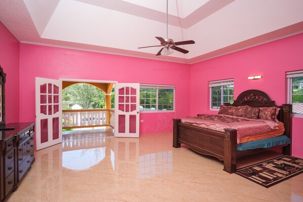 A bedroom with pink walls, a wooden bed, a ceiling fan, and a balcony with a railing.