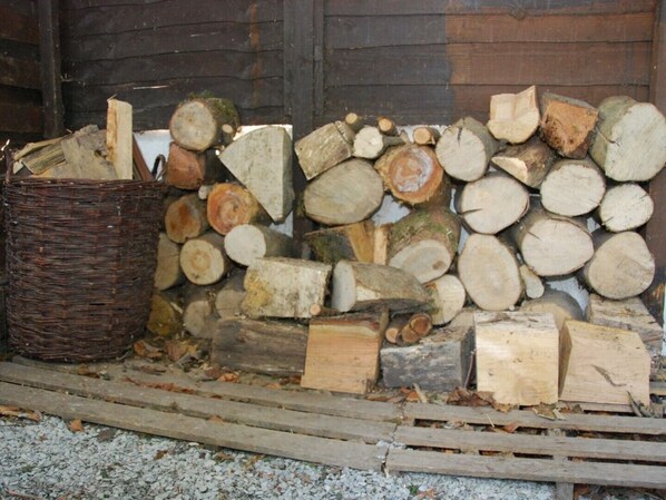 A stack of firewood and a wicker basket against a wooden wall.