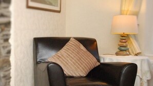 Un fauteuil en cuir noir avec un coussin à rayures, une petite table avec une lampe et un tableau encadré au mur.