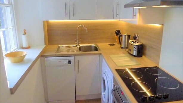 Une cuisine compacte équipée d’un lave-vaisselle, d’un lave-linge et d’une plaque de cuisson à induction noire.
