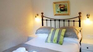 Un lit bien fait, recouvert d’une couvre-lit à motifs floraux, avec deux oreillers et deux serviettes pliées posées sur le lit.