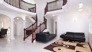 A spacious living area with a black leather sofa, a patterned rug, and a wooden staircase with a railing.