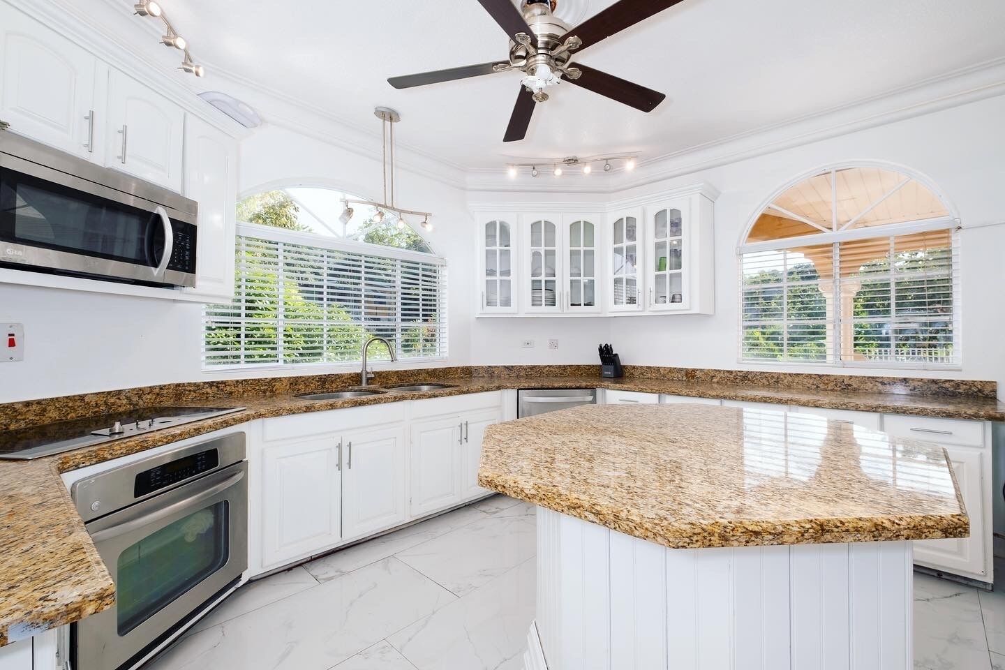 A modern kitchen with white cabinetry, granite countertops, a built-in oven, and a ceiling fan.