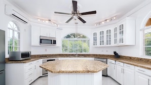 A kitchen with white cabinetry, a granite countertop, a ceiling fan, and a window with a view of greenery.