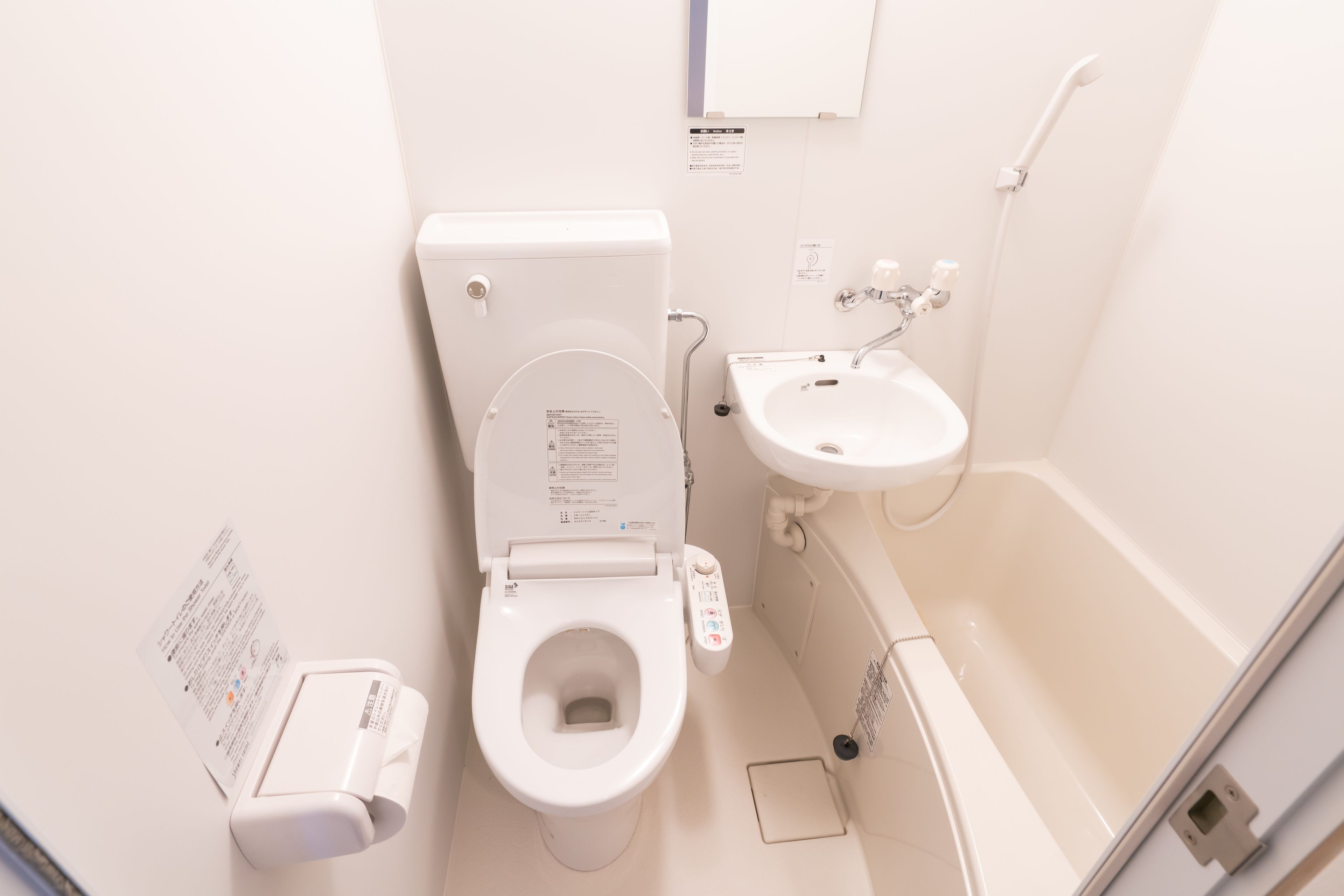 A small, white bathroom with a toilet, sink, and shower.