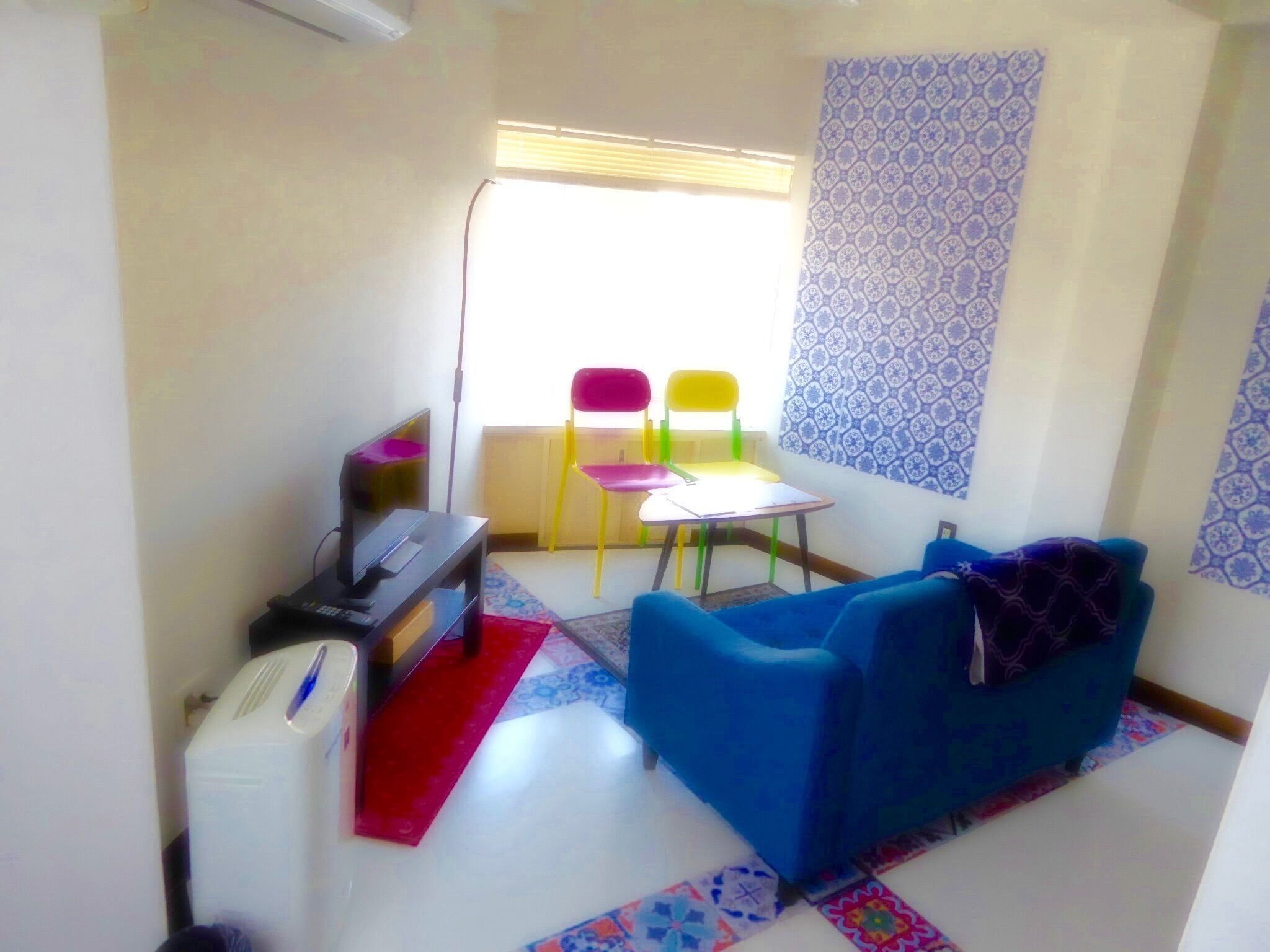 A small, brightly lit room with a blue sofa, a small table, and colorful chairs.