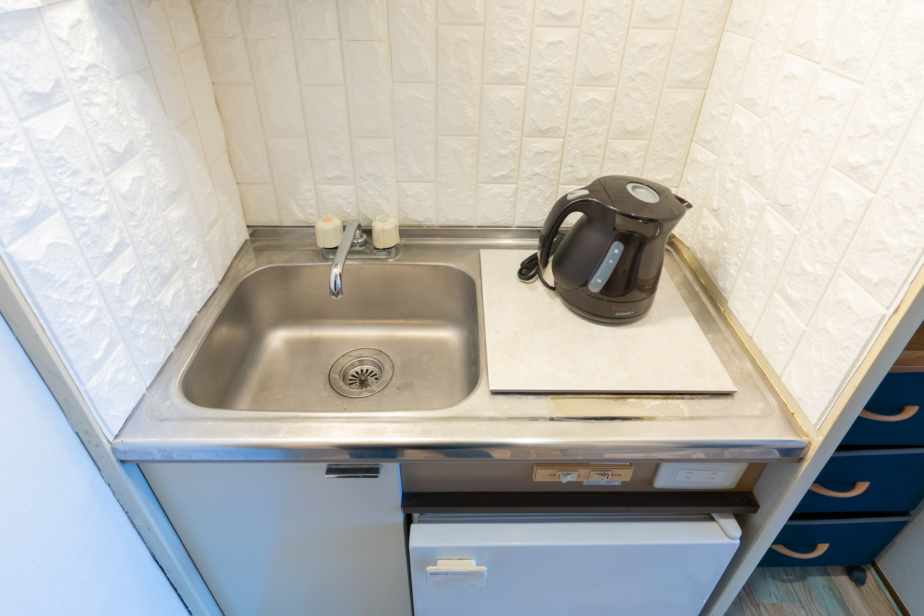 Eine kleine Küche mit Edelstahlspüle, Wasserkocher und kleinem Kühlschrank.