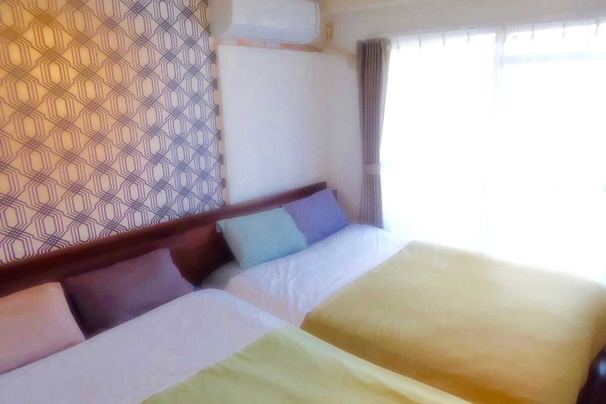 Ein Hotelzimmer mit zwei Betten, einer Wand mit Muster und einem Fenster mit Vorhängen.
