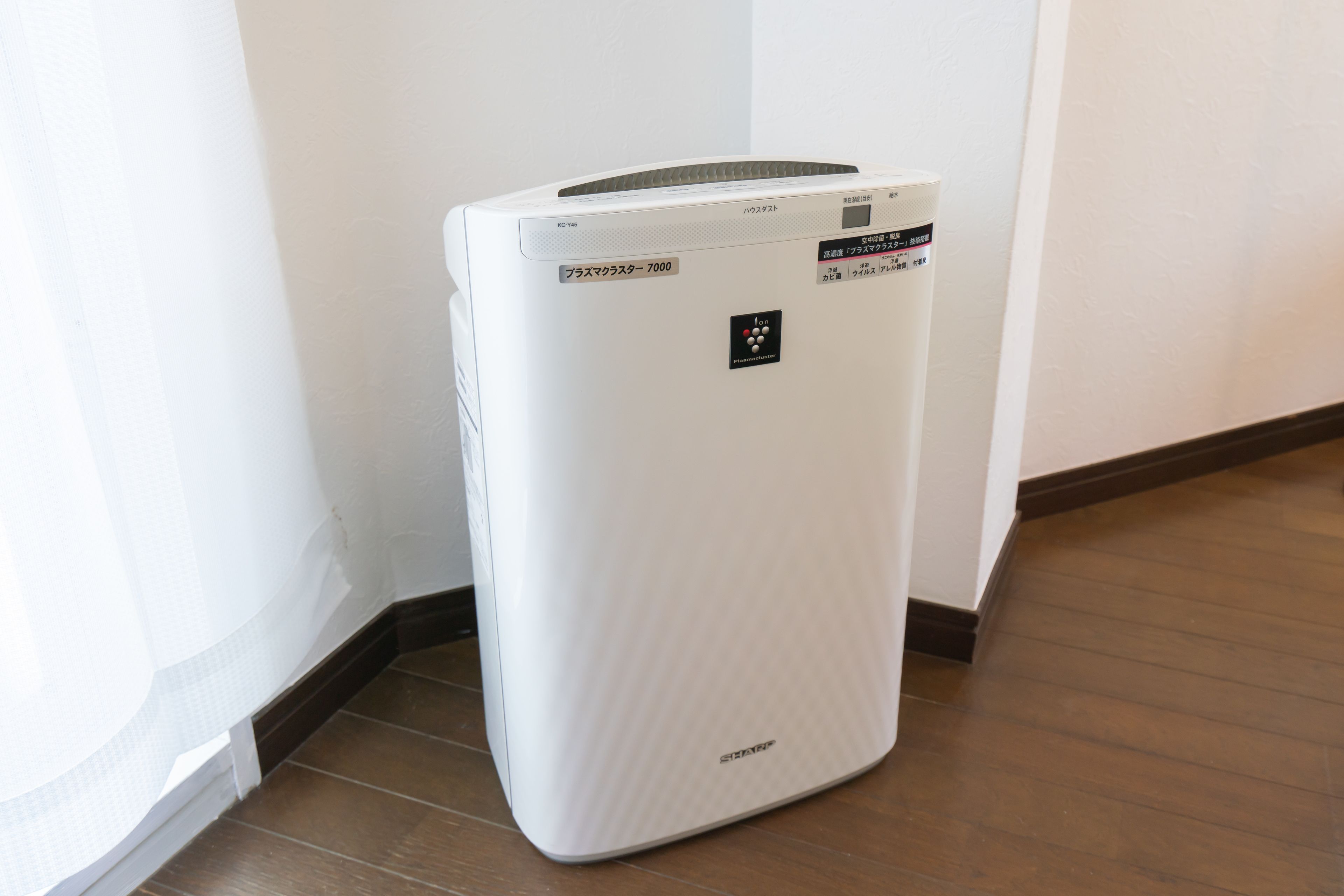 A white portable air conditioner with a control panel and a brand logo on the front, placed on a wooden floor against a white wall.