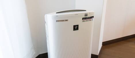 A white portable air conditioner with a control panel and a brand logo on the front, placed on a wooden floor against a white wall.