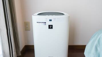 A white portable air conditioner with a control panel, placed on a tiled floor next to a wall socket.