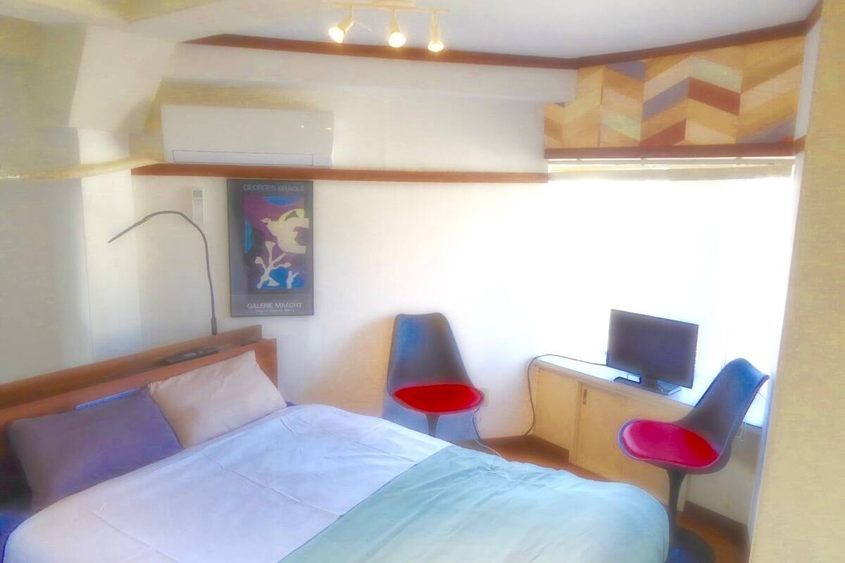 Ein Hotelzimmer mit einem Bett, einem Schreibtisch mit Computer, zwei Stühlen und einer Wandklimaanlage.