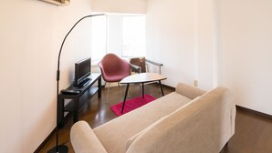 Uma sala de estar moderna com um sofá, uma televisão, uma poltrona vermelha e uma pequena mesa.