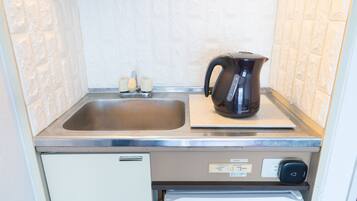 A compact kitchen with a stainless steel sink, a black electric kettle, and a built-in refrigerator.